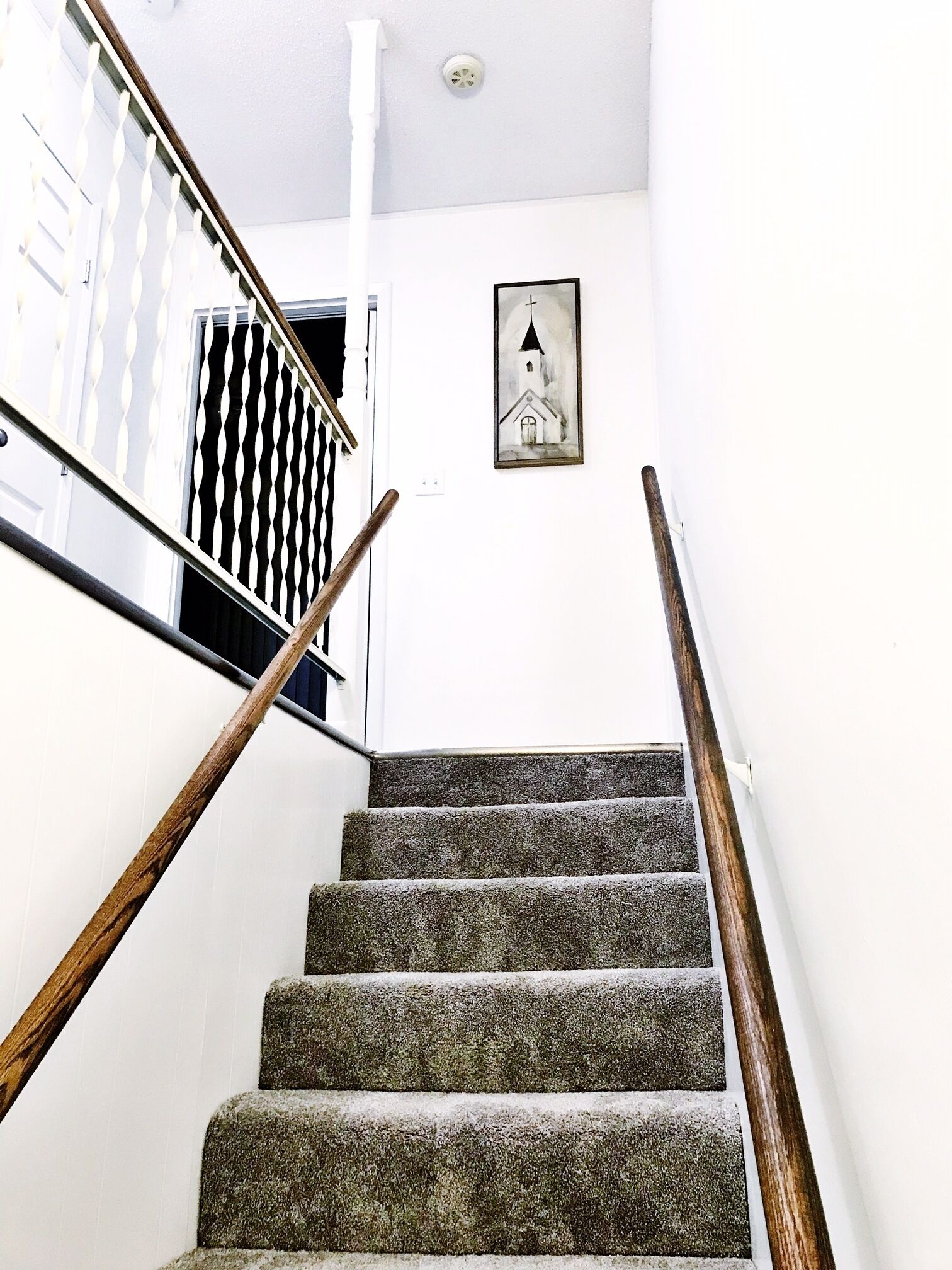 Una escalera con barandillas de madera y un cuadro de una iglesia en la pared.