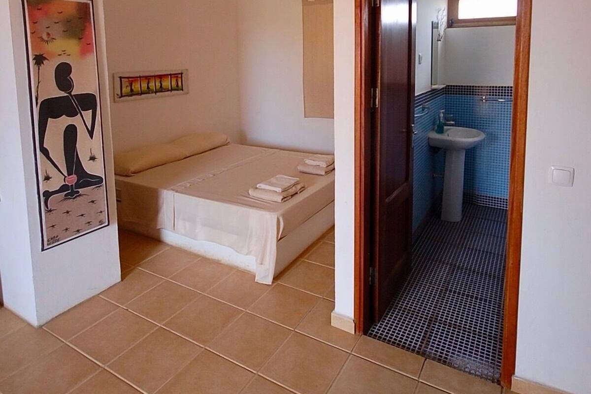 Une chambre à coucher avec un lit, une petite salle de bain avec un lavabo et une porte donnant sur une autre pièce.