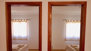 Um quarto refletido em um espelho, com cama, cortinas e piso de azulejos.