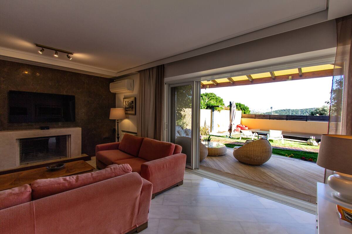 A modern living room with a fireplace, sofas, and a large sliding glass door leading to an outdoor area.