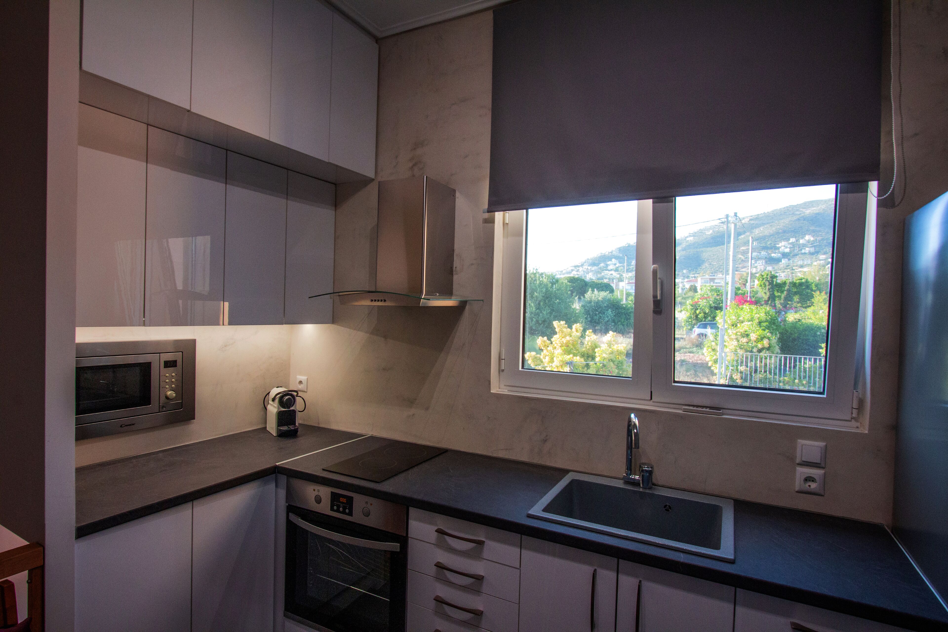 A modern kitchen with a built-in microwave, oven, and sink, with a window offering a view of greenery and hills.