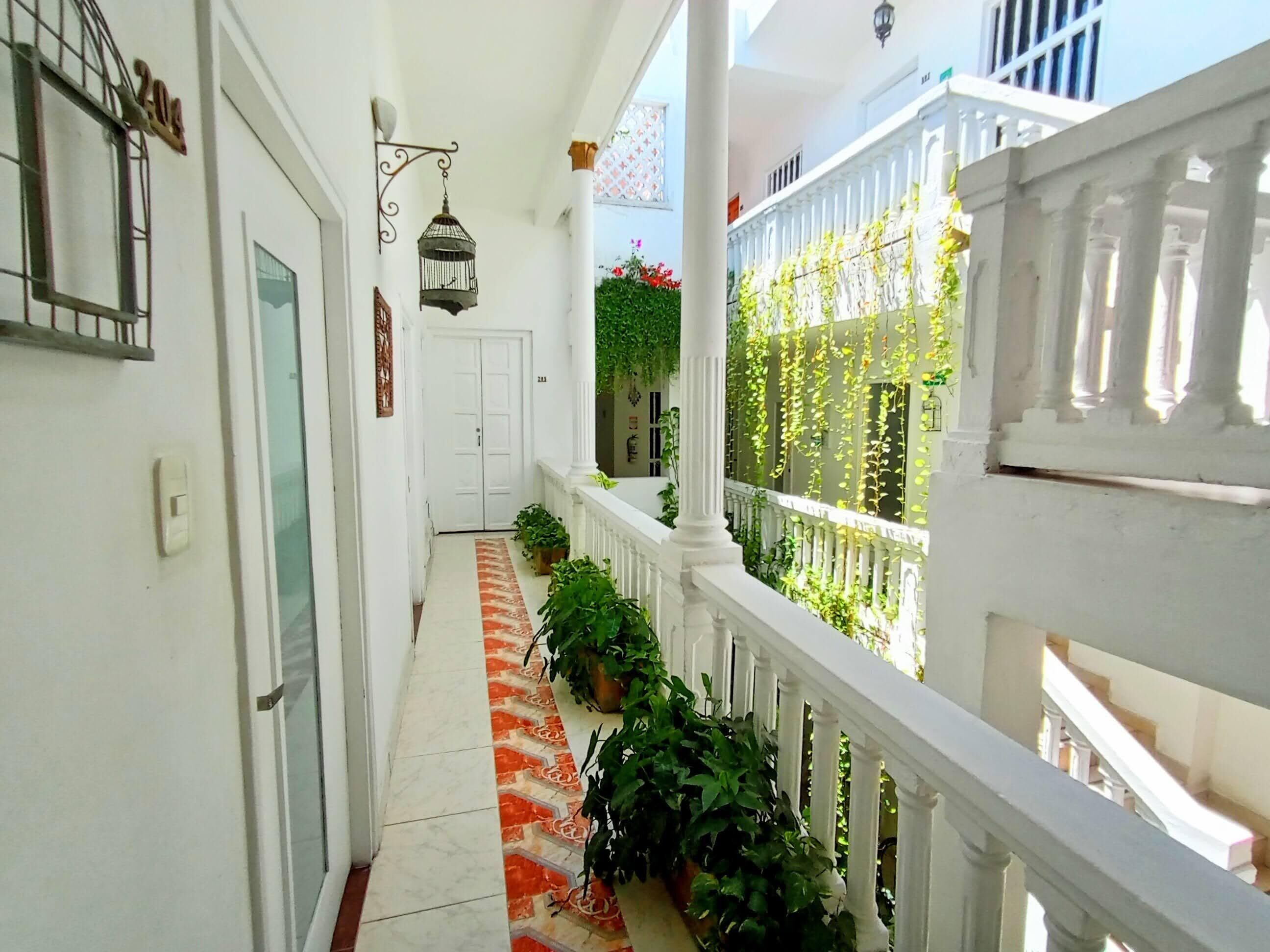 A corridor with a tiled floor, white walls, a white door, and a white railing with greenery.