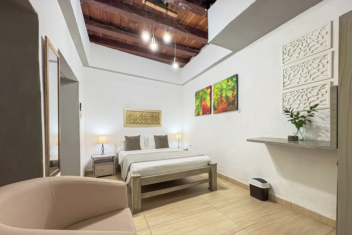 Un dormitorio moderno con cama, mesitas de noche, una silla y obras de arte en las paredes.