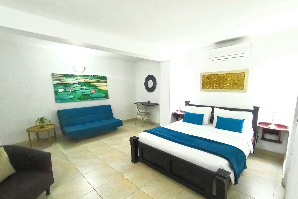 Un dormitorio con cama, un sofá azul, una mesita y un aire acondicionado de pared.