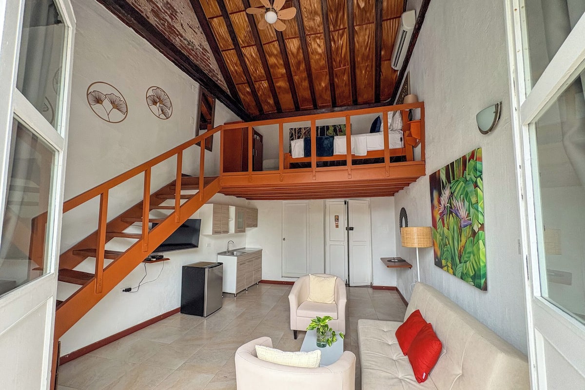 Un salón espacioso con una escalera de madera, un sofá, una mesa de centro y un cuadro en la pared.