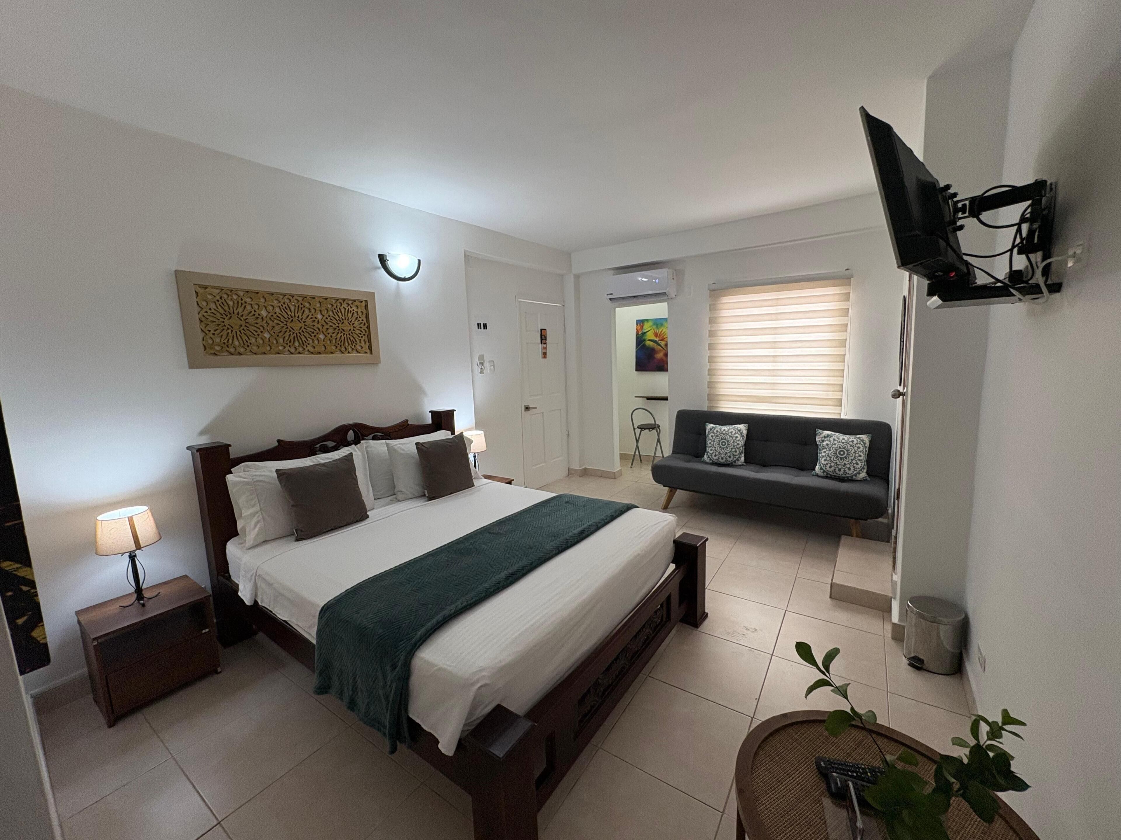 A bedroom with a bed, bedside table, lamp, and a TV mounted on the wall.