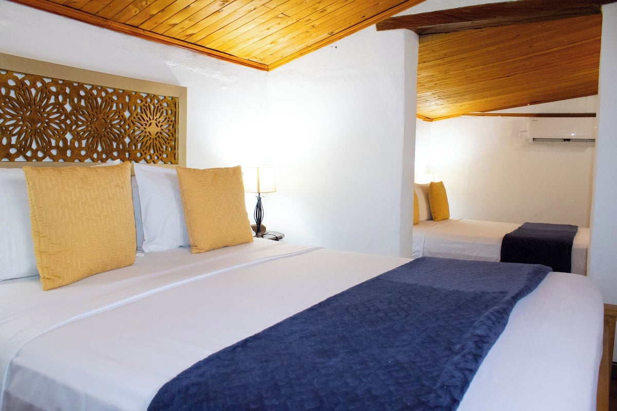 Habitación de hotel con dos camas, un cabecero decorativo, una lámpara de noche y un equipo de aire acondicionado.