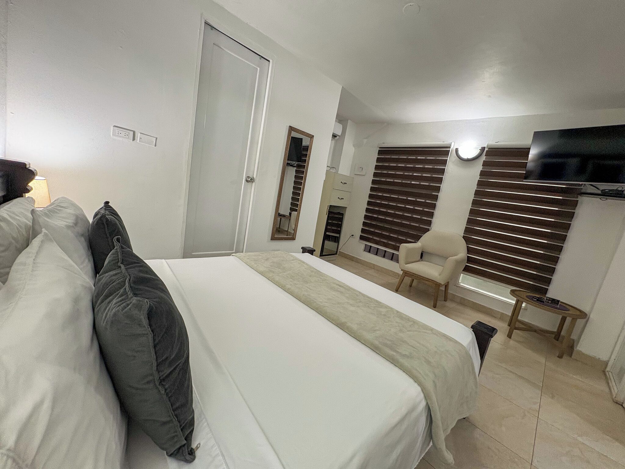 A bedroom with a bed, a chair, a TV, and a window with blinds.