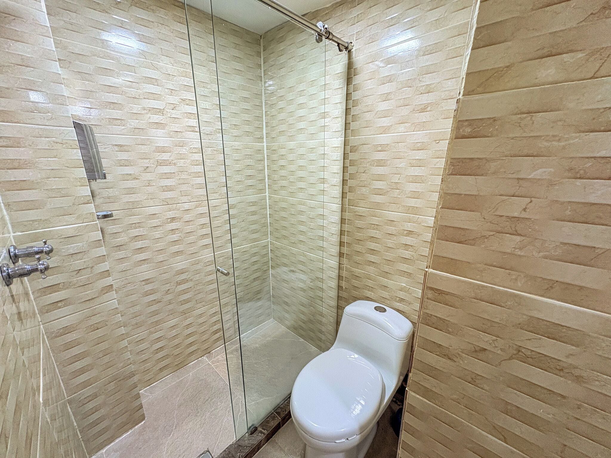 Un baño con ducha de vidrio, inodoro y paredes con azulejos.