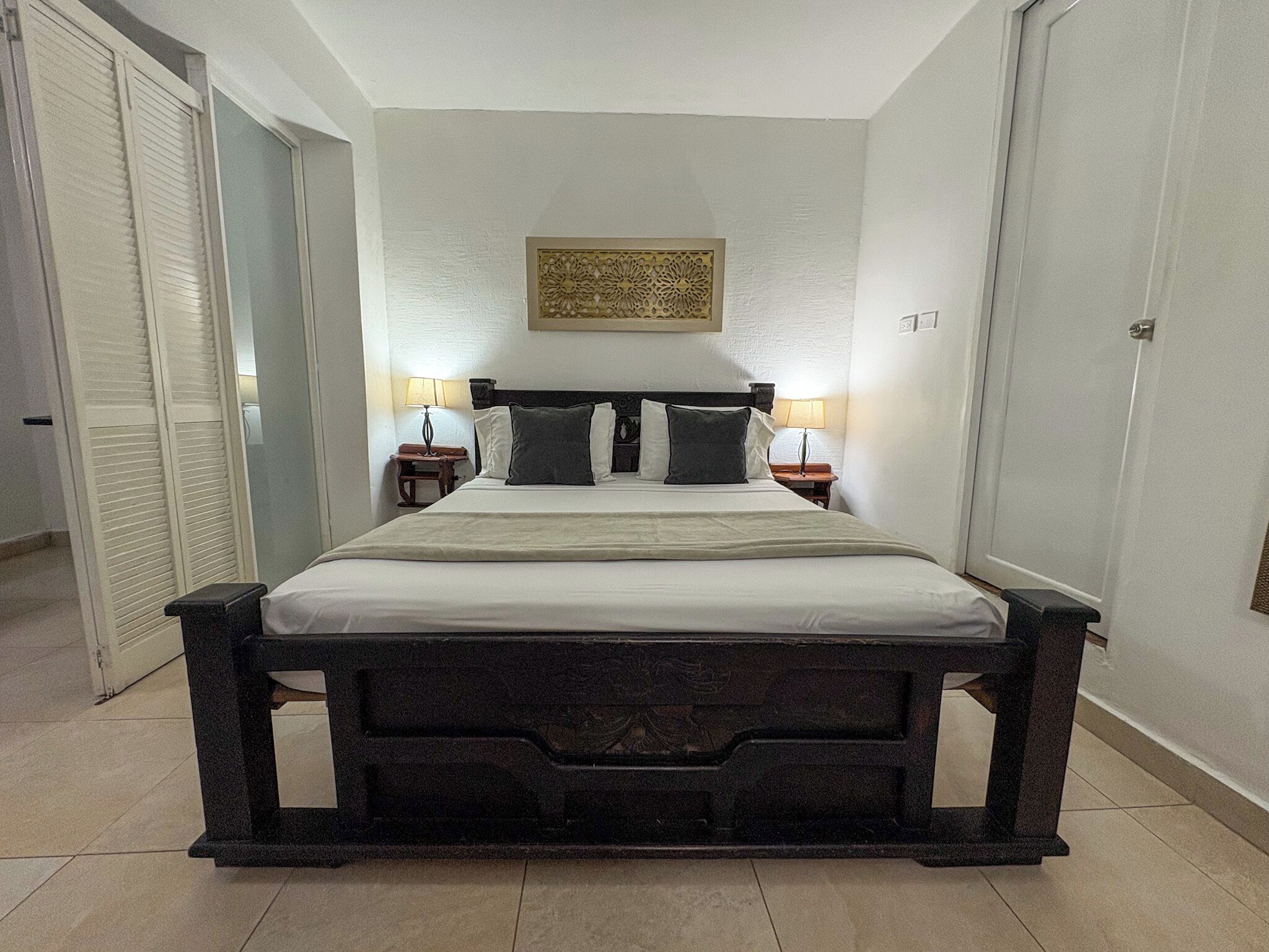 A neatly arranged bed with a headboard, two bedside tables with lamps, and a decorative wall piece above the bed.