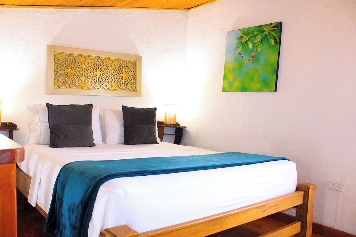 Un dormitorio con una cama, dos mesitas de noche, un panel decorativo y un cuadro.