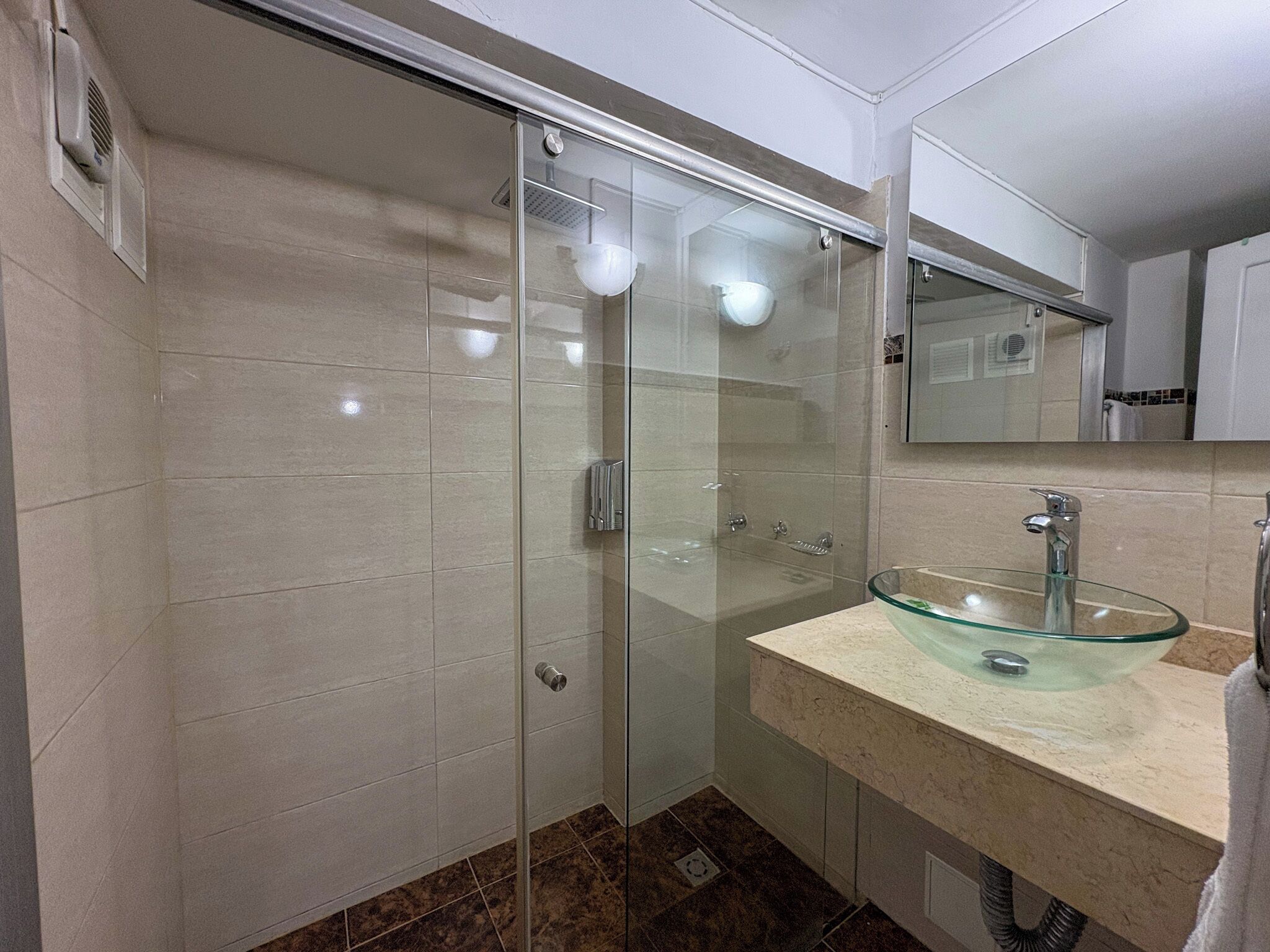 A modern bathroom with a glass shower enclosure, a glass sink, and a large mirror.