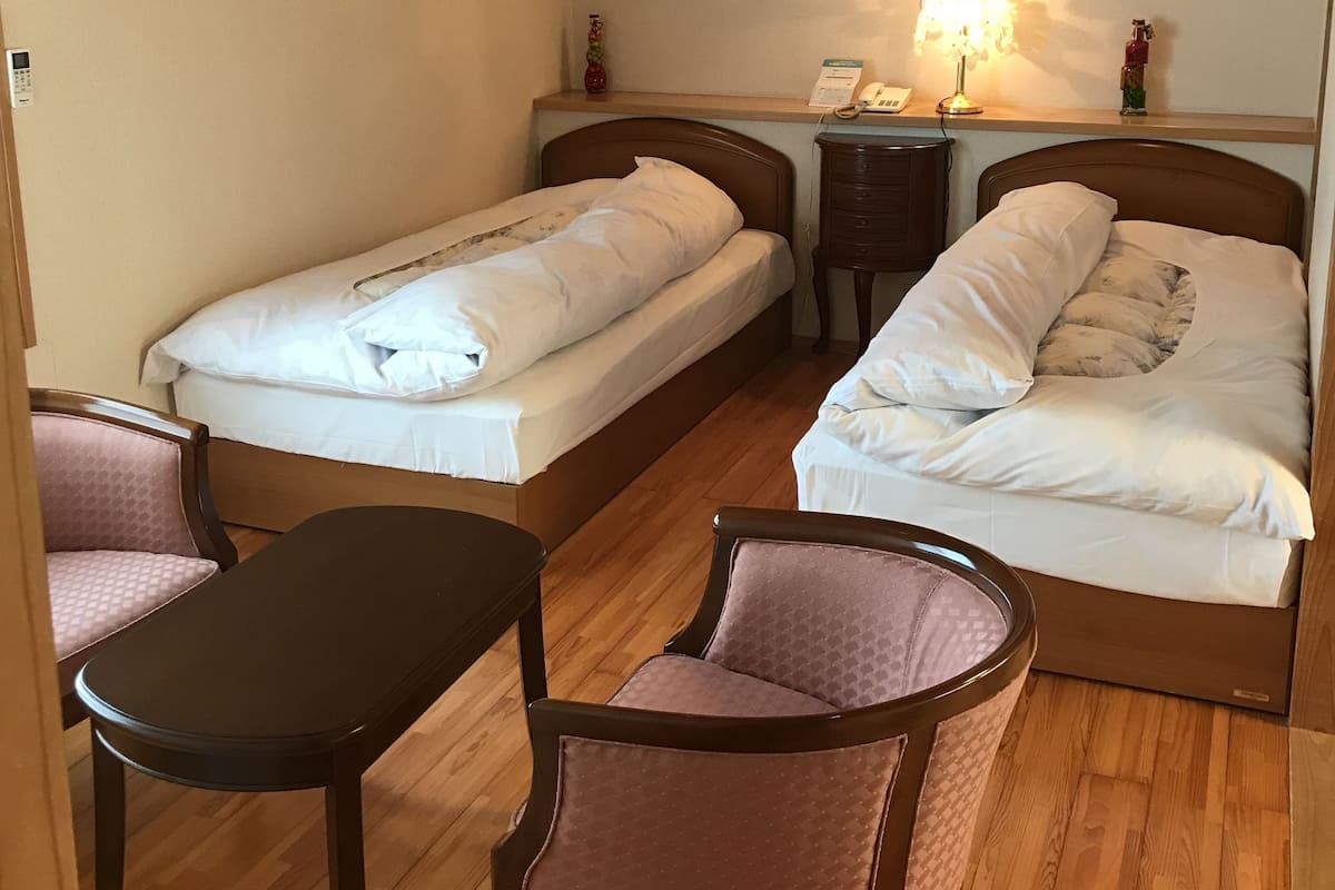 Una habitación pequeña y acogedora con dos camas individuales, un escritorio, una silla y una mesita de noche.