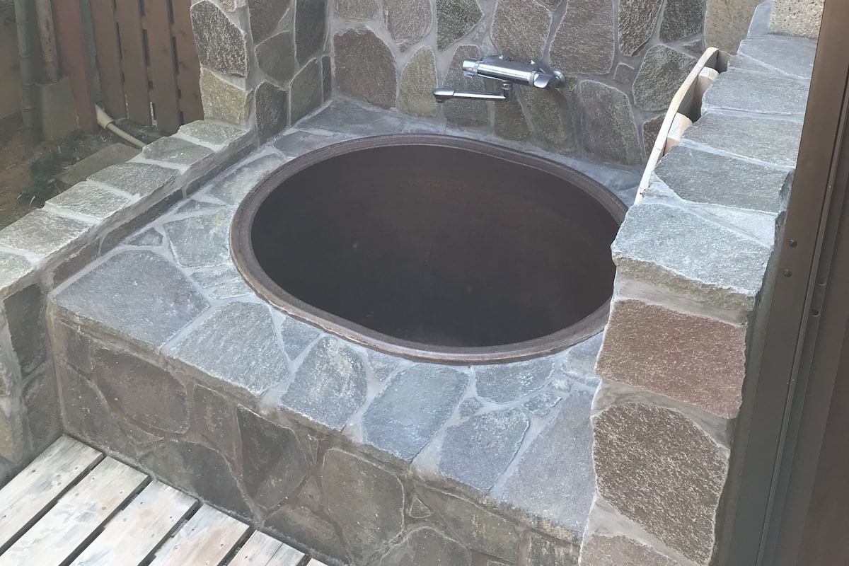 Tinaja de piedra con pared de piedra y valla de madera al fondo.