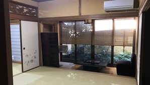 A traditional Japanese room with tatami flooring, a sliding door, a window with blinds, and an air conditioning unit. - Ritouen (Ureshino)