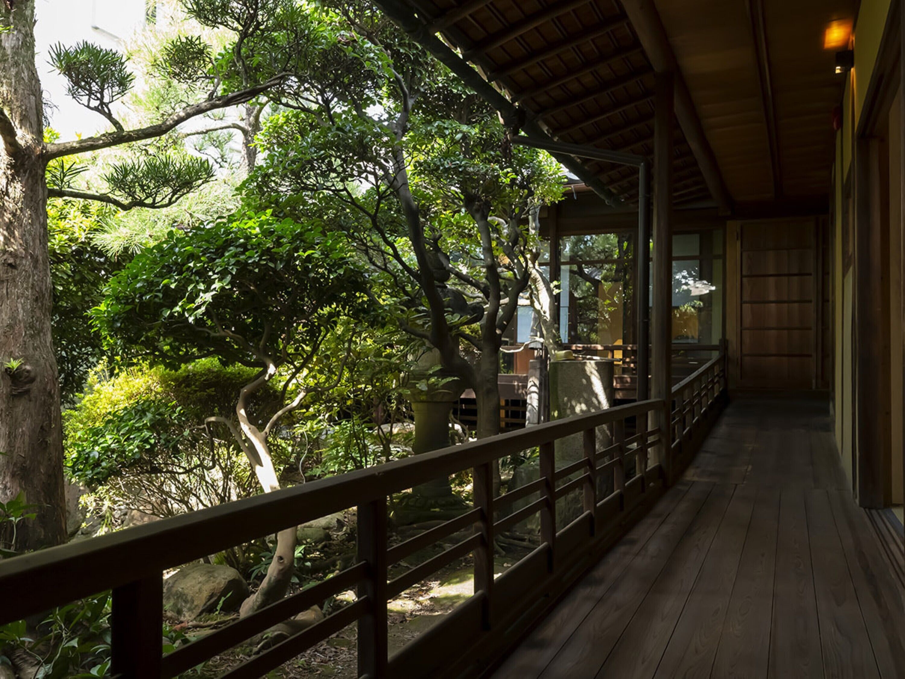A wooden deck with a railing overlooking a garden with trees and a building in the background.