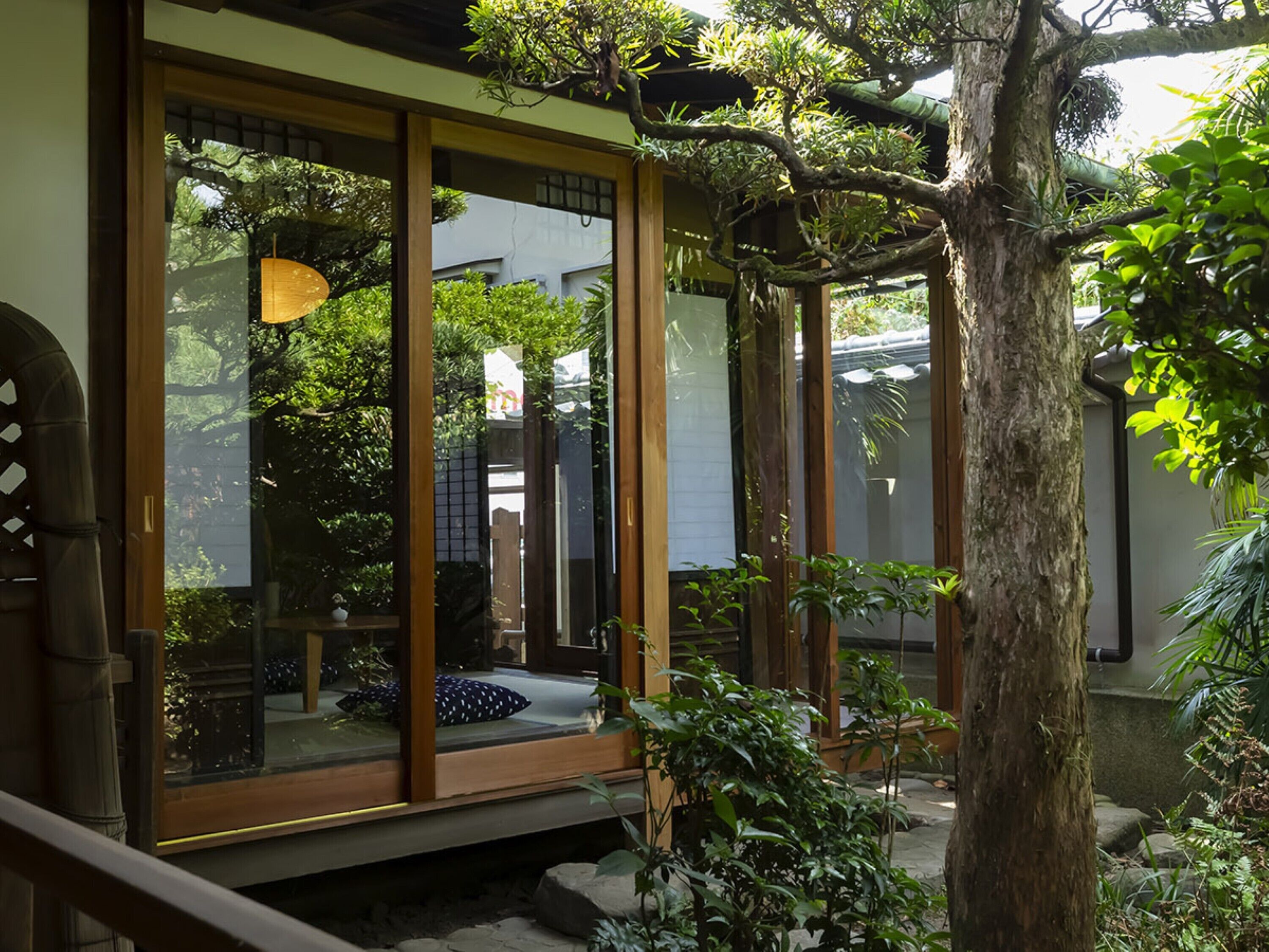 A traditional Japanese-style room with sliding doors, a tatami mat floor, and a view of a garden with trees and a pond.