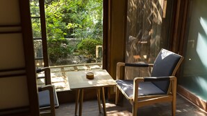 A room with a wooden table and chairs, a view of greenery outside, and a sliding glass door. - Kazeno Naramachi (Nara)