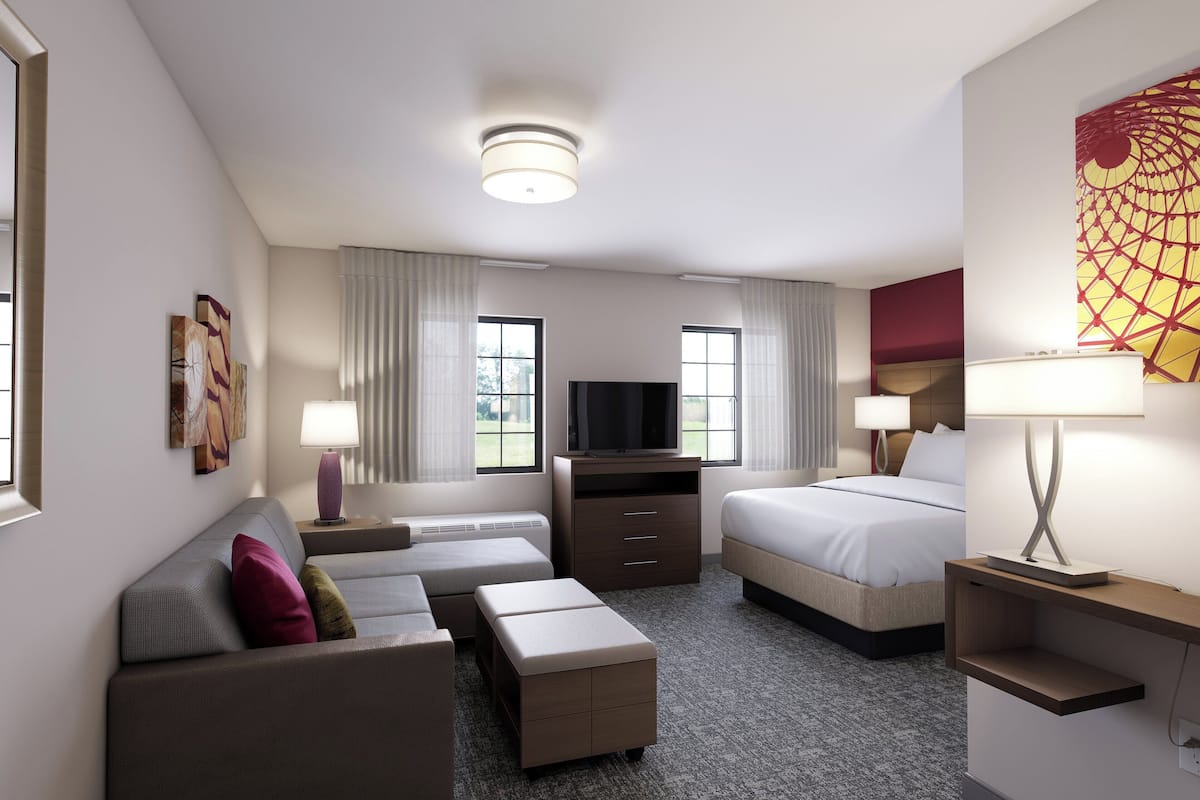 A modern hotel room with a sofa, a bed, a TV, and a desk with a lamp.