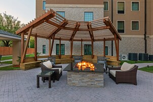 Un patio exterior con una chimenea, asientos y una estructura de pérgola.