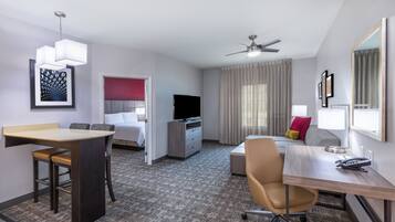 A hotel room with a desk, chair, bed, television, and a ceiling fan.