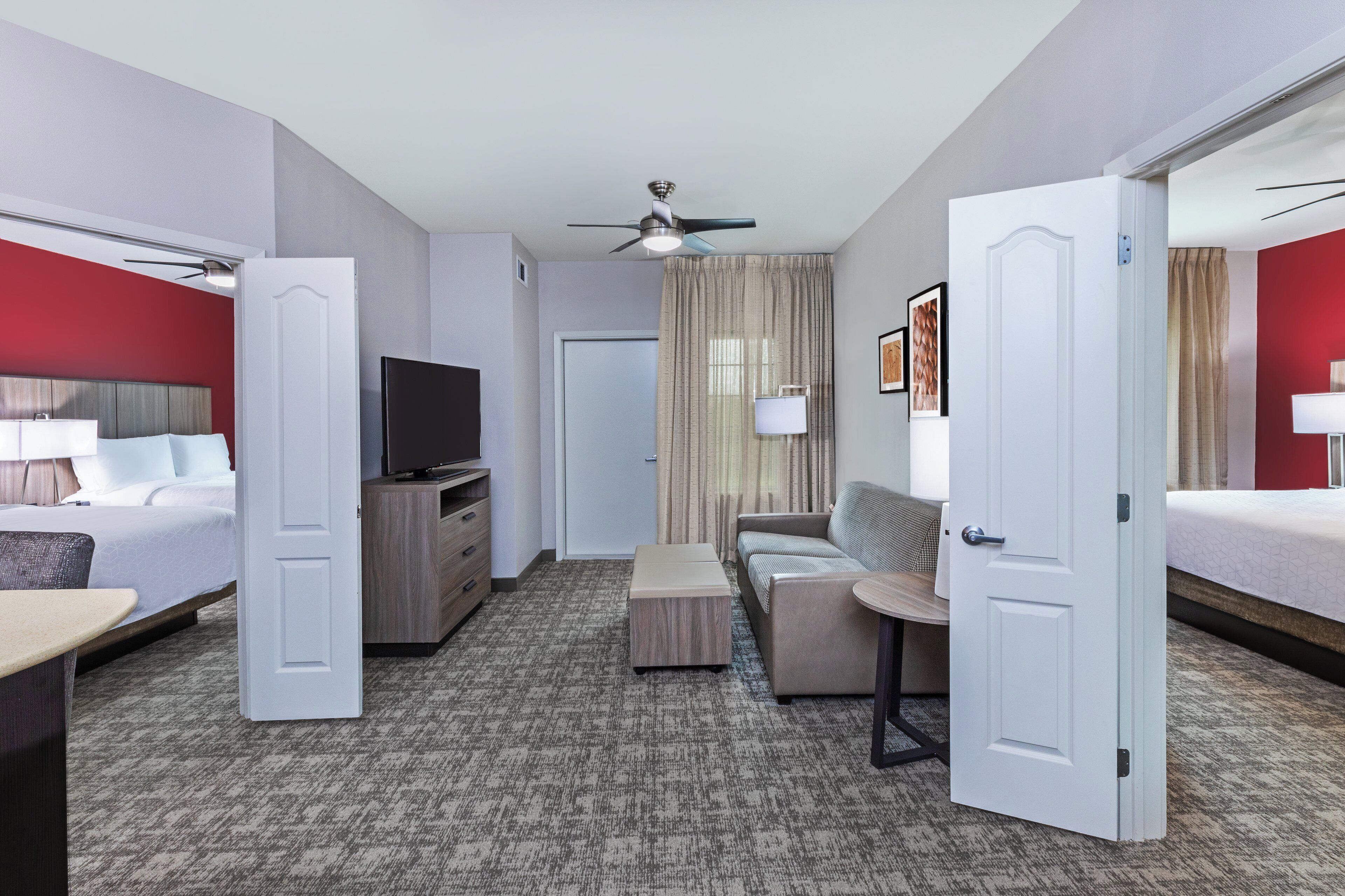 A hotel room with a bed, a TV, a sofa, a desk, and a ceiling fan.