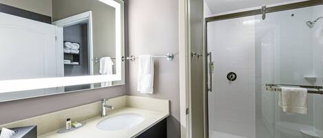 Un baño con ducha de mampara de vidrio, lavamanos con espejo y perchero para toallas.