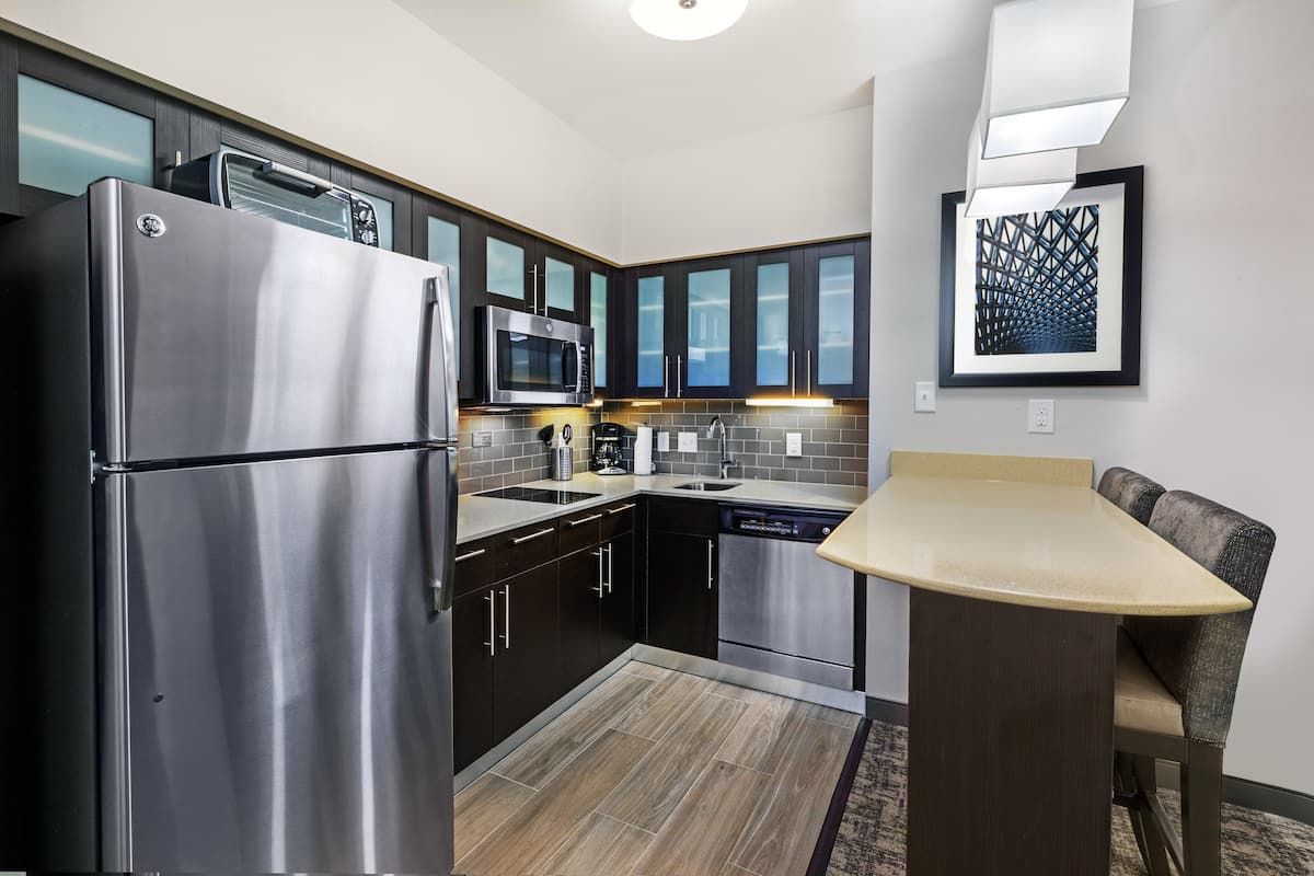 A modern kitchen with dark cabinets, stainless steel appliances, a dishwasher, and a dining area with a bench.