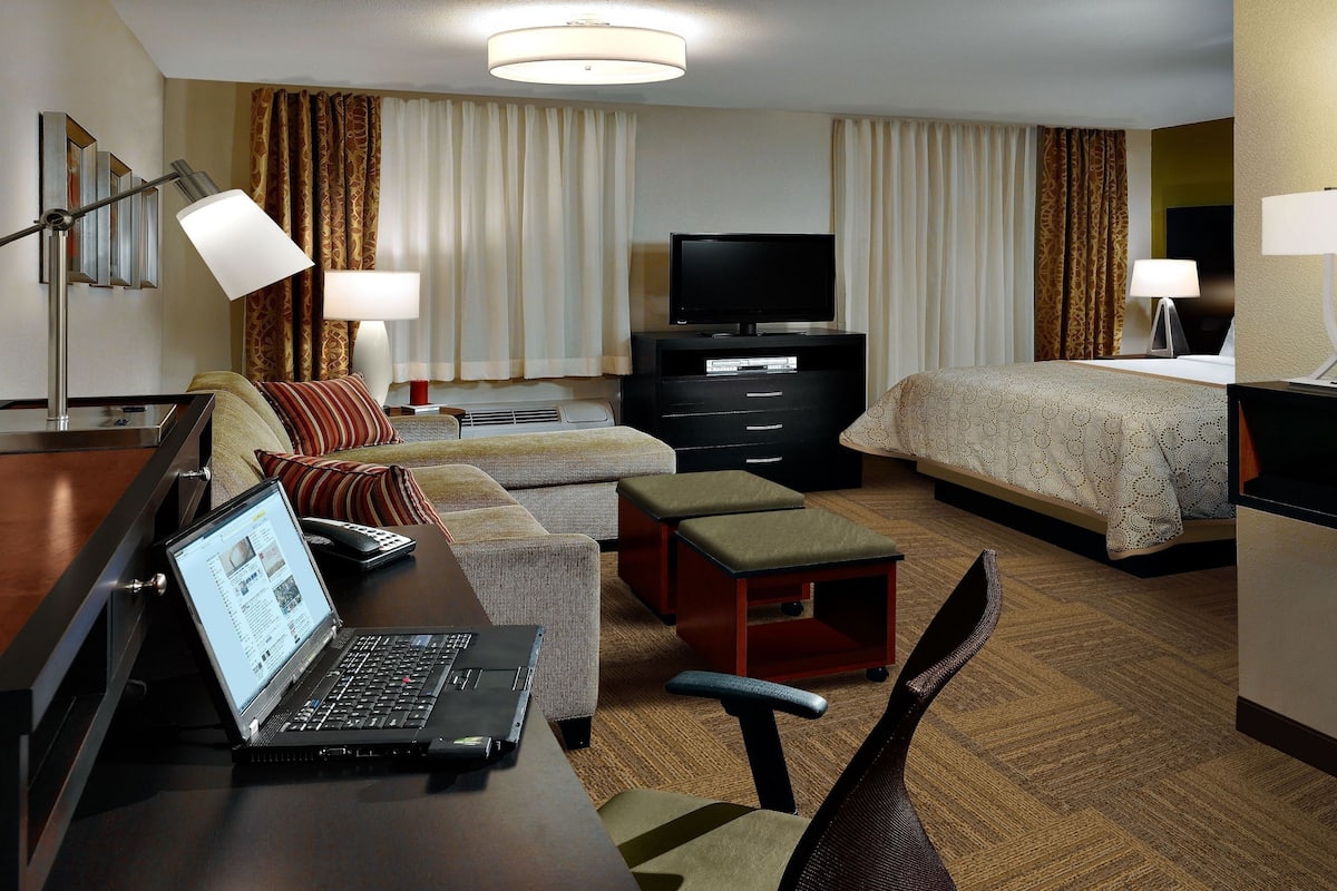 Een hotelkamer met een bed, een bank, een bureau met een laptop, een televisie en een bureaulamp.