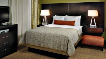 A hotel room with a bed, two bedside tables with lamps, a television on a dresser, and a carpeted floor.