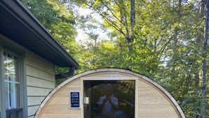 A wooden sauna with a glass door, located on a wooden deck with a house in the background. - Enjoy private...beautiful… large house with outdoor hot tub and sauna ! (Slaty Fork)