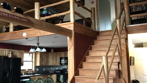 A cabin interior with a wooden staircase, a dining area, kitchen, and a loft with a sign reading "COME TO OUR CABIN". - Enjoy private...beautiful… large house with outdoor hot tub and sauna ! (Slaty Fork)