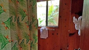 A room with a wooden door, a window with a view of greenery, and a tiled floor. - Evergreen Cottage by Maui Adventure Villa (Haiku-Pauwela)