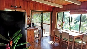 A wooden interior with a kitchen, dining area, and large windows. - Evergreen Cottage by Maui Adventure Villa (Haiku-Pauwela)