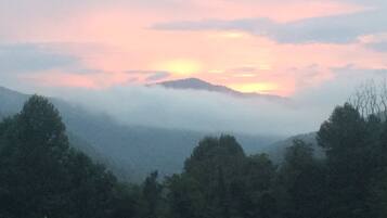 A mountainous landscape with a forested foreground and a sunset in the background.