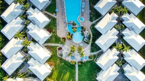 Vista aérea de un complejo turístico con varias edificaciones de techo blanco, una piscina central y palmeras circundantes.