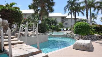 A pool area with stone steps, lounge chairs, and palm trees.