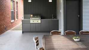 Un espace cuisine extérieur avec un mur en briques, un plan de travail gris et une table en bois avec des chaises.