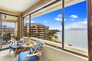 Un balcó amb cadires de vimet i una taula, amb vistes a una platja i un edifici d'hotel.