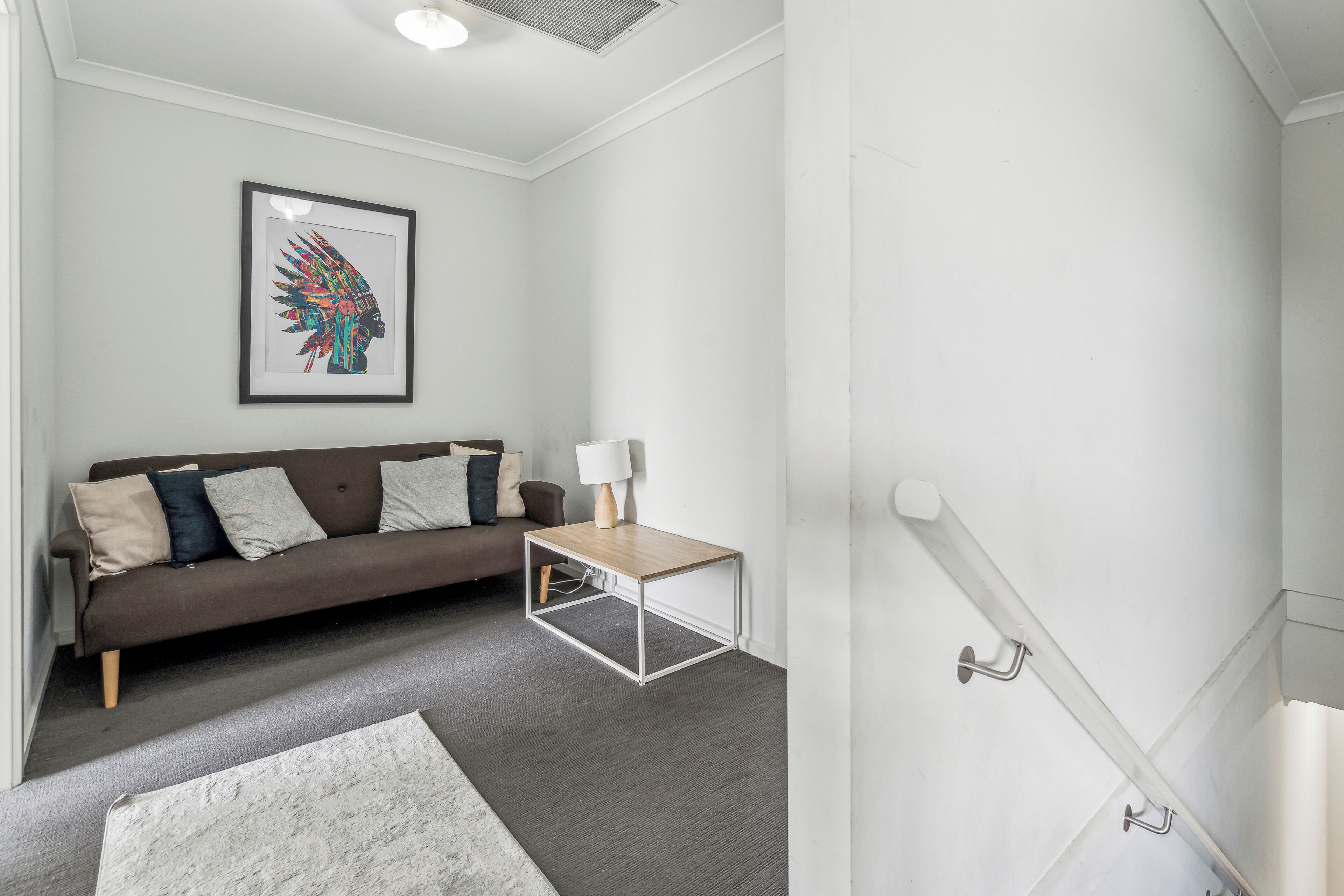 A modern living room with a brown sofa, a small wooden coffee table, and a framed artwork on the wall.