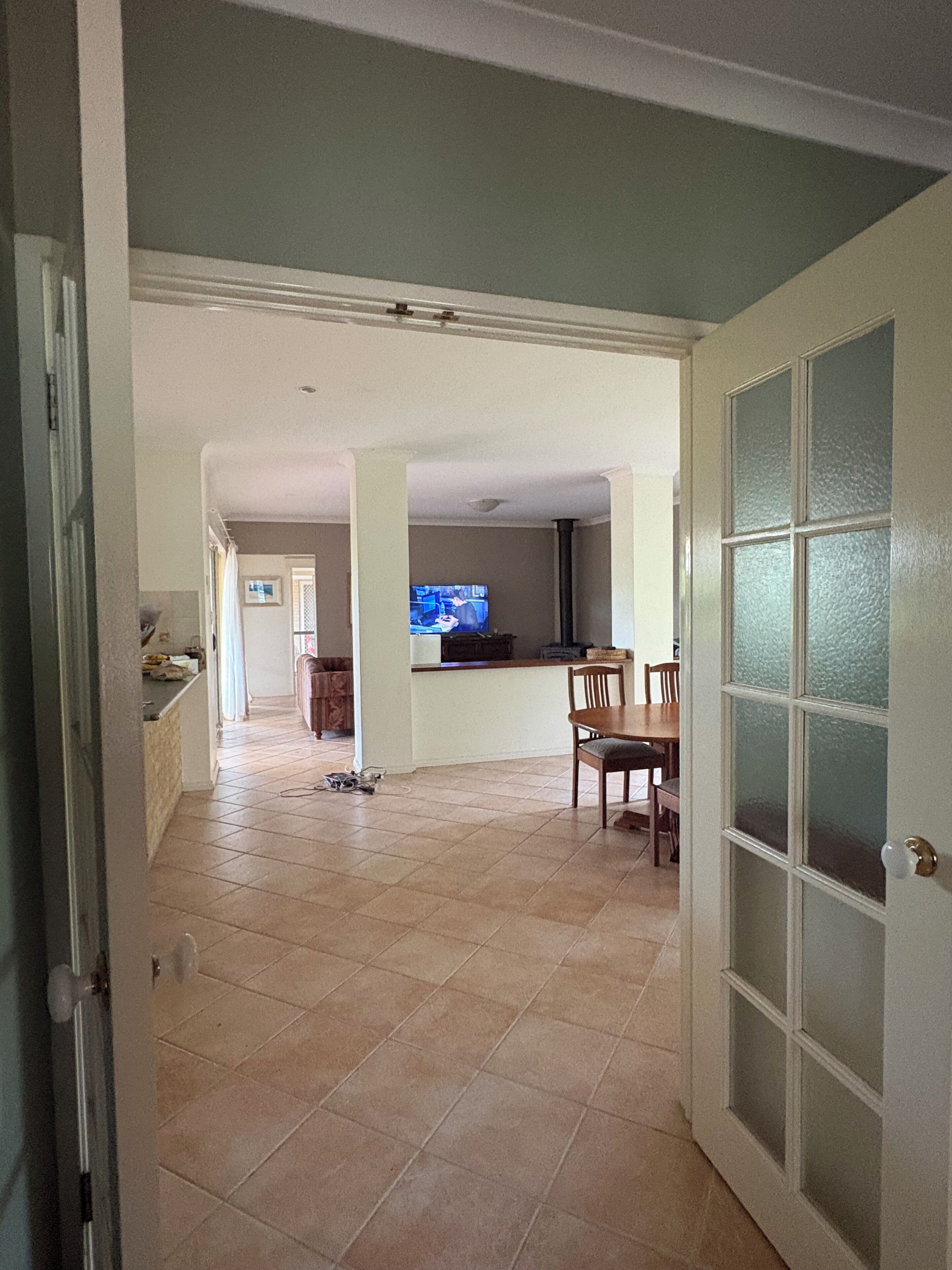 A spacious living area with a dining table and chairs, a television, and a kitchen area visible in the background.