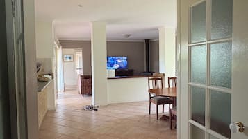 A spacious living area with a dining table and chairs, a television, and a kitchen area visible in the background.