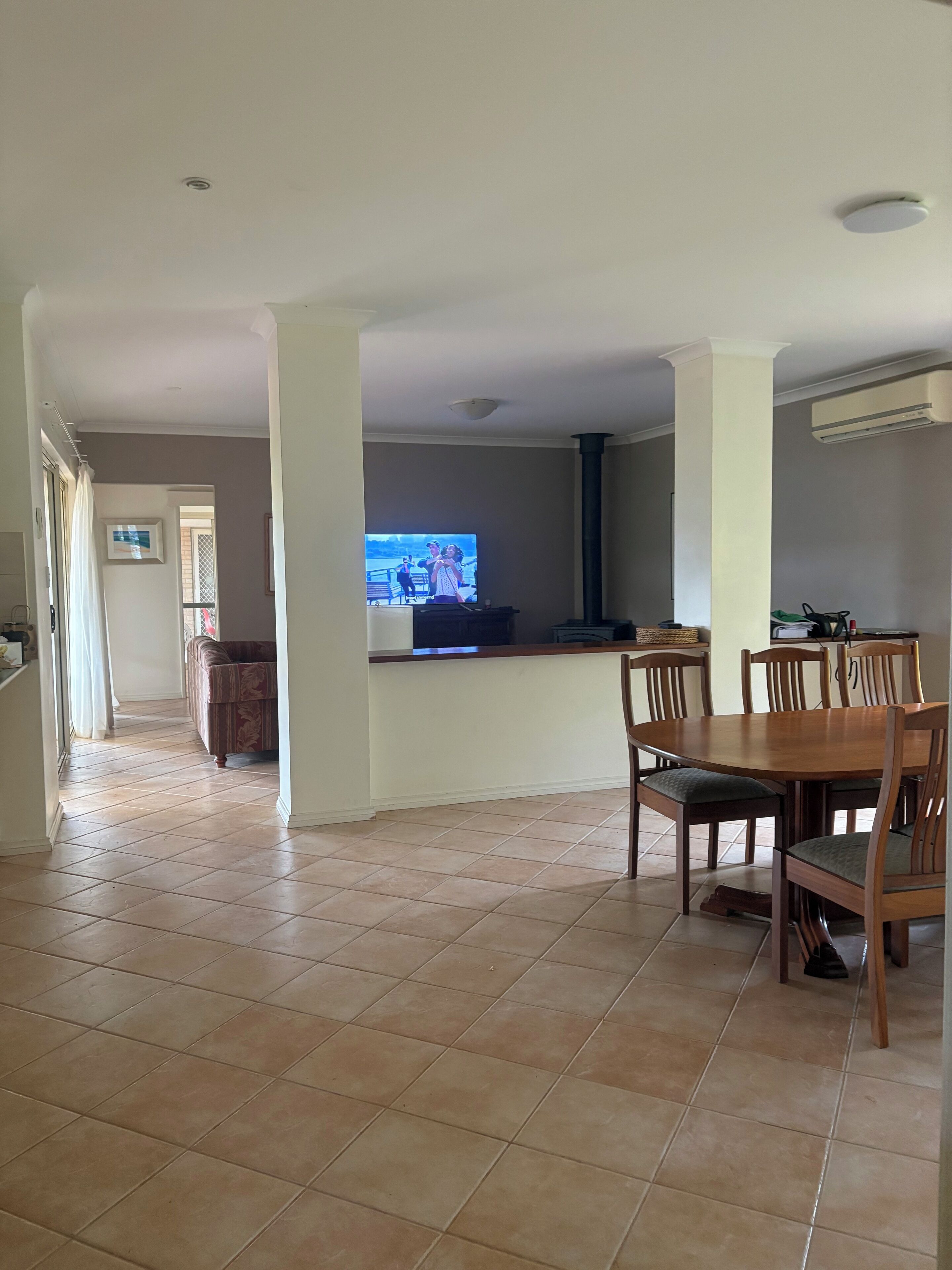 A spacious living area with a dining table and chairs, a TV in the background, and a kitchen area with a stove and chairs.
