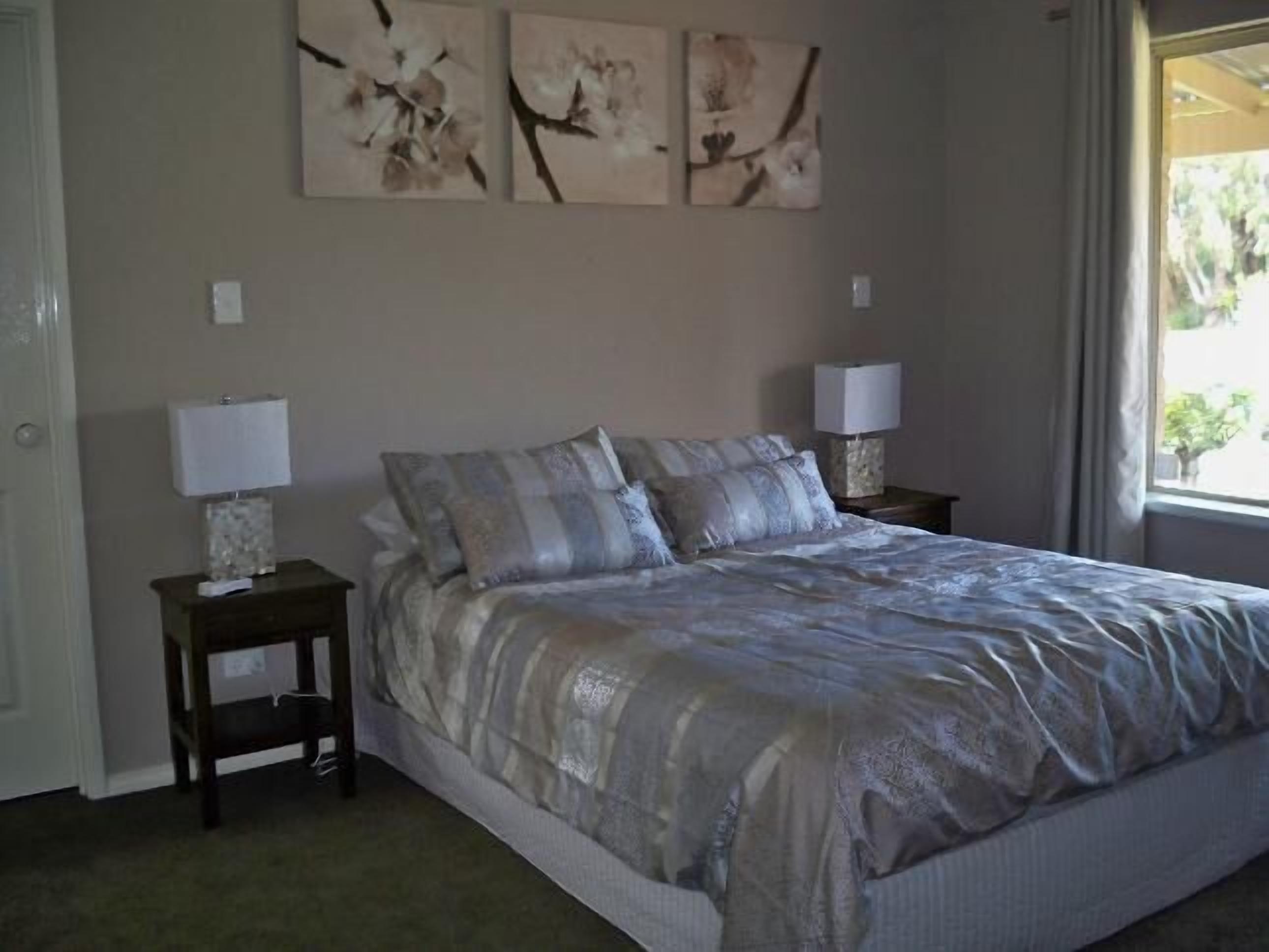 A bedroom with a large bed, two bedside tables with lamps, and three wall-mounted artworks.