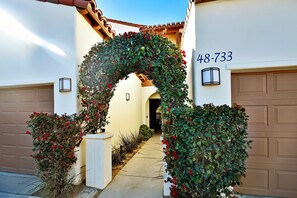 Una entrada de casa con un arco decorativo cubierto de follaje y flores rojas, que lleva a un garaje con el número 48-733.