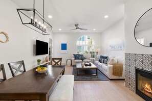 Una sala de estar moderna con chimenea, un comedor con mesa de madera y una zona de estar con sofá y sillones.