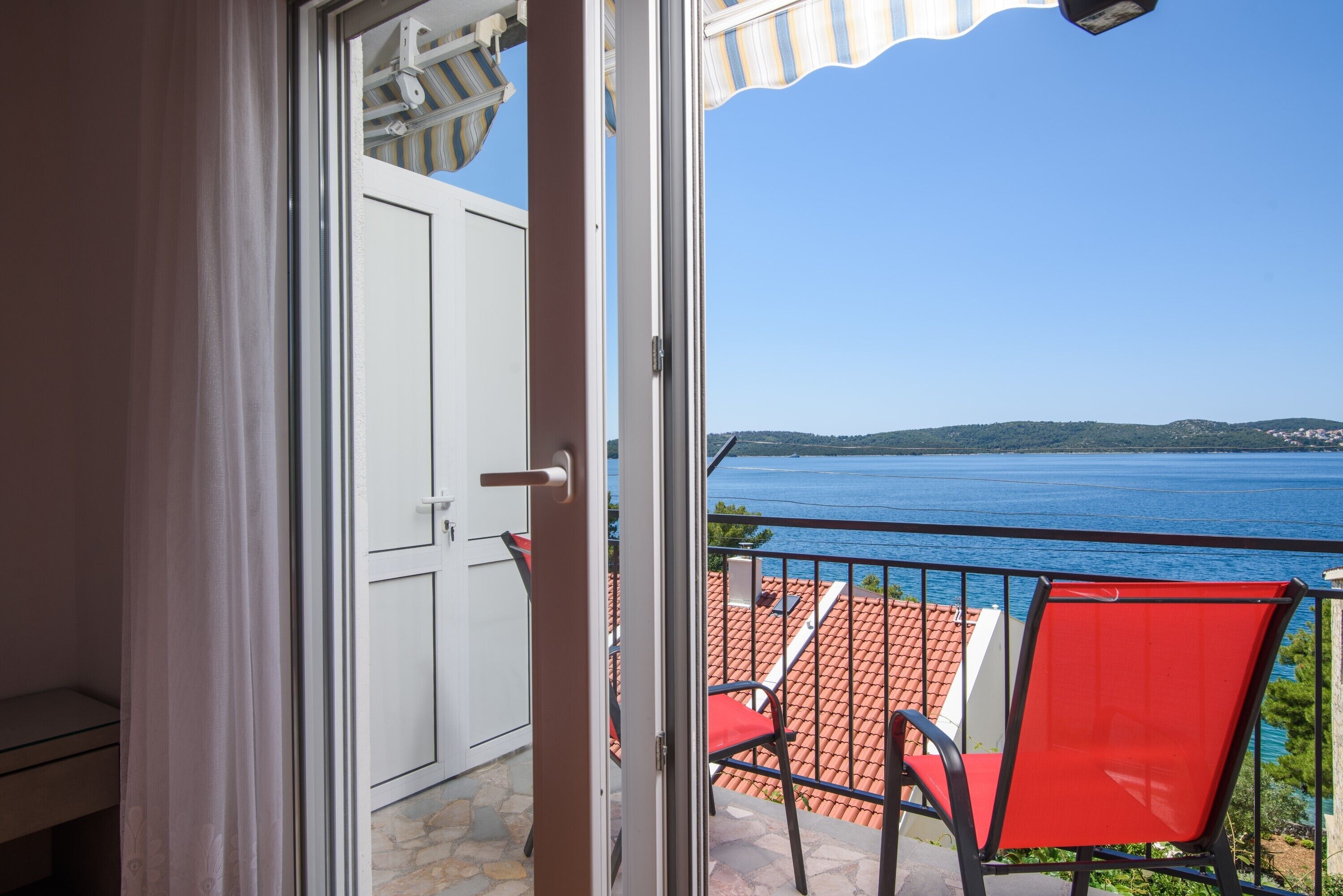 A balcony with a red chair, a view of the sea, and a tiled roof.
