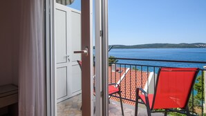 Un balcón con una silla roja, vista al mar y tejado de baldosas.