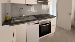 Una cocina moderna con armarios blancos, un lavamanos de acero inoxidable, lavavajillas y horno.
