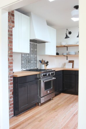 A kitchen with black cabinets, a wooden countertop, a gas stove, and a brick wall.